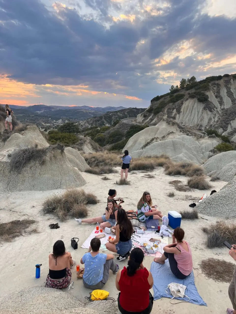 Group of travelers relaxing on rocky badlands terrain at sunset