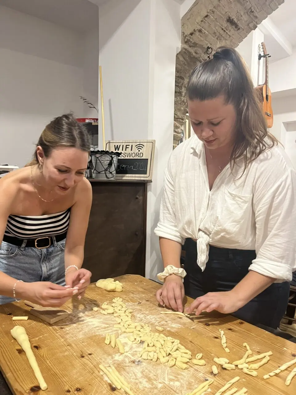 Two women preparing handmade pasta shapes on a wooden table