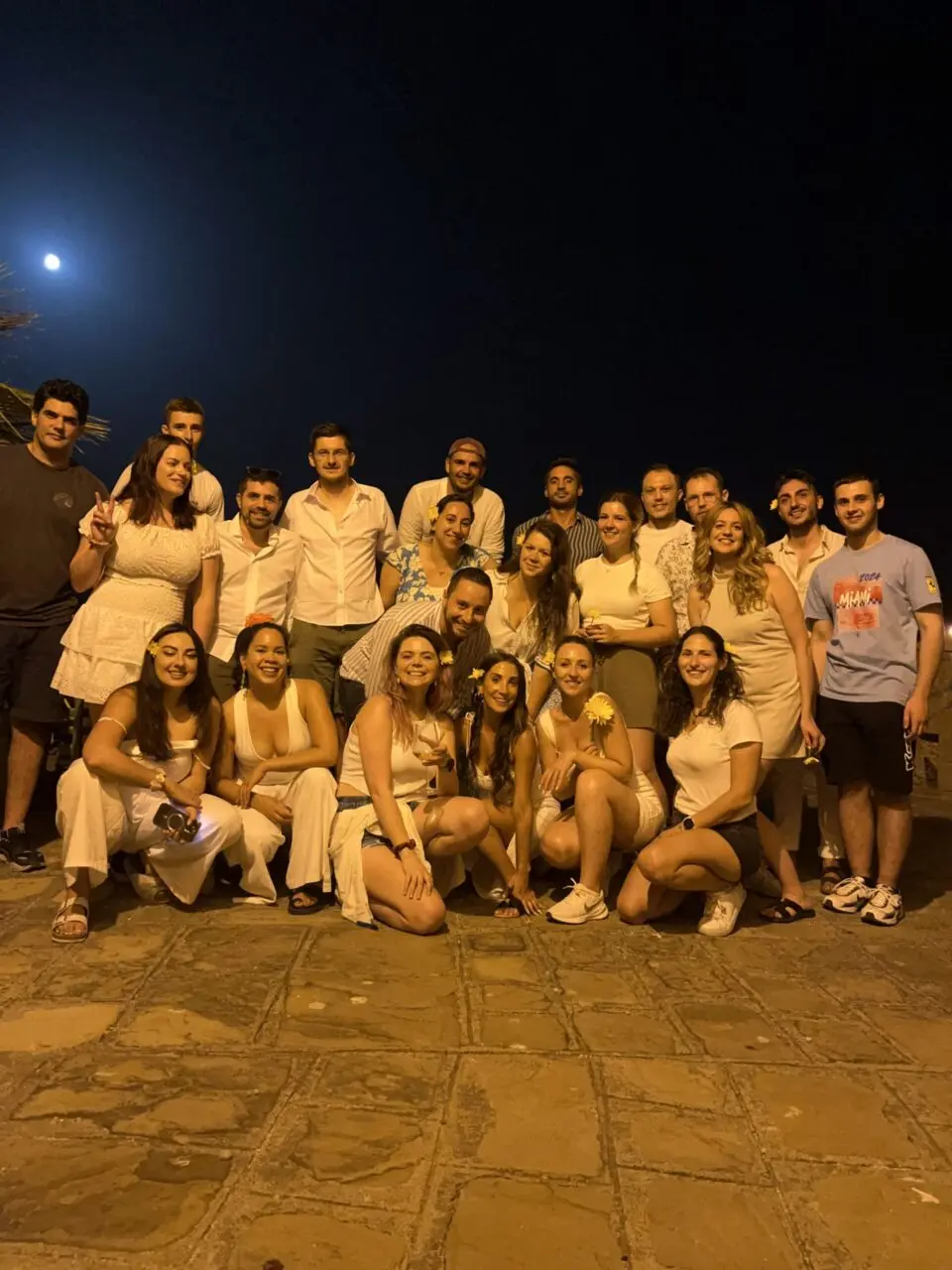 Large group posing together on a rooftop terrace at night under a full moon