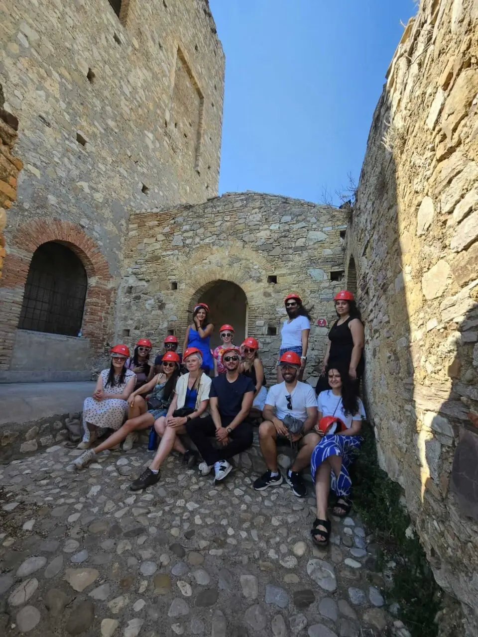 Group of friends posing with red helmets in a stone archway during a tour