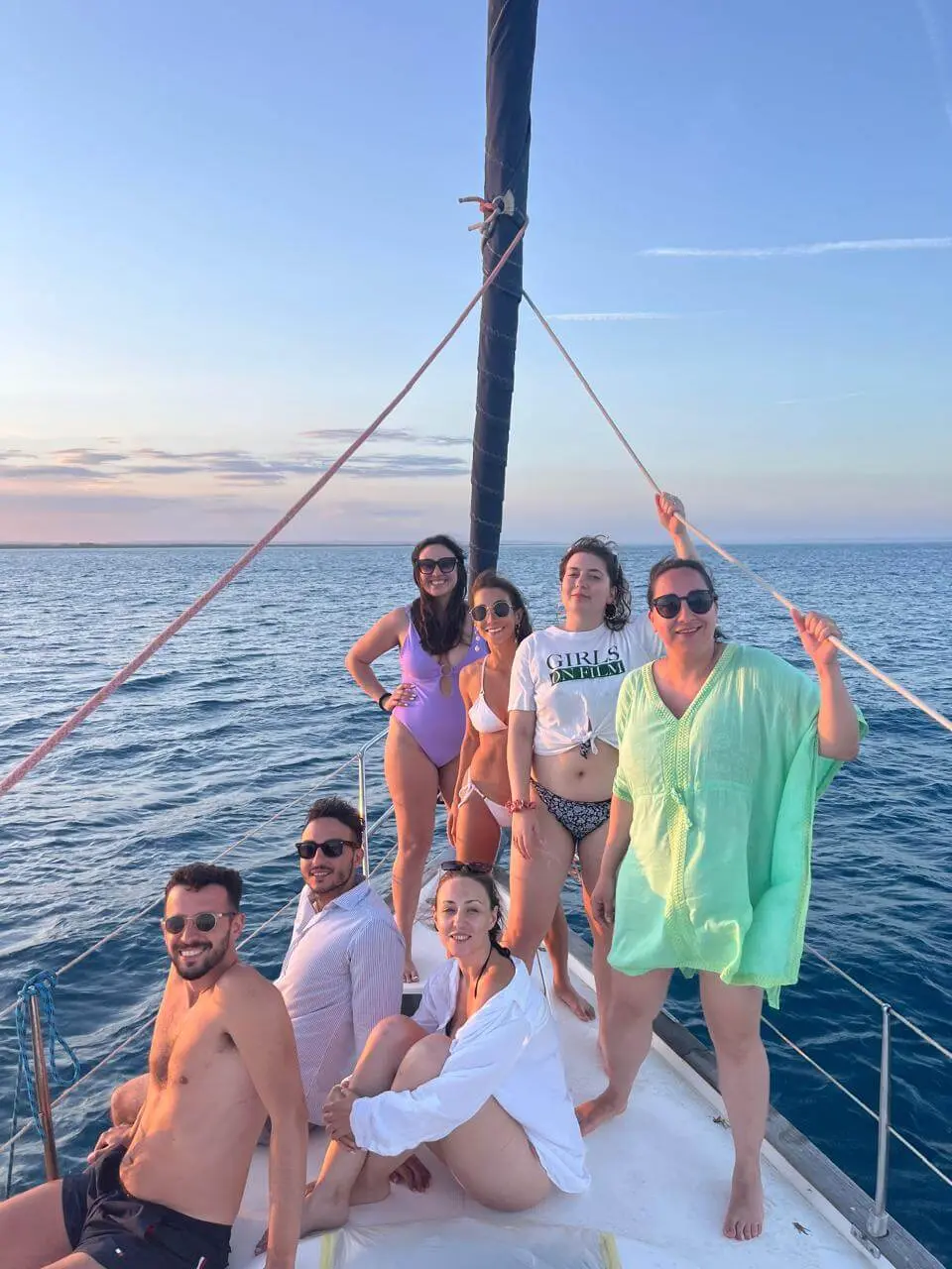 Group of friends sailing on a boat at sunset, some in swimwear